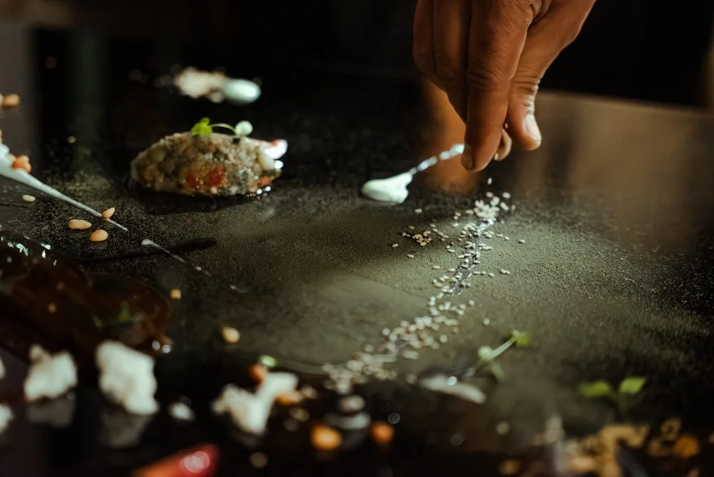 La main du chef sème une pluie de sel sur une assiette sombre